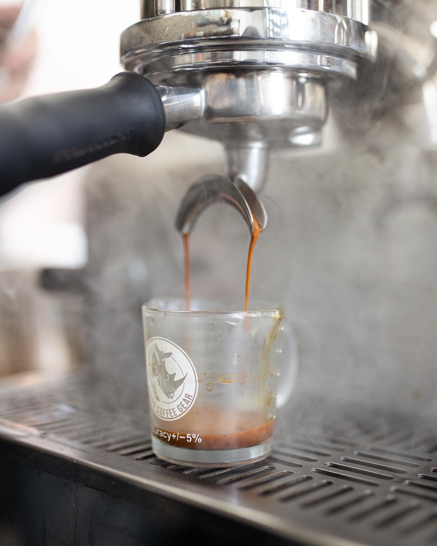 Espresso pouring from a portafilter into a glass, steam rising.